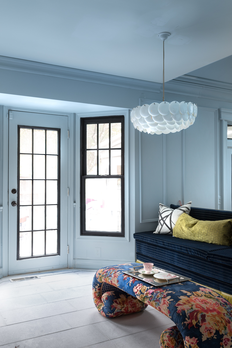 parma blue walls with Metrie Moulding, upholstered banquette, marble floors with a black pinstripe, and waterfall coffee table with Original BTC lighting fixture