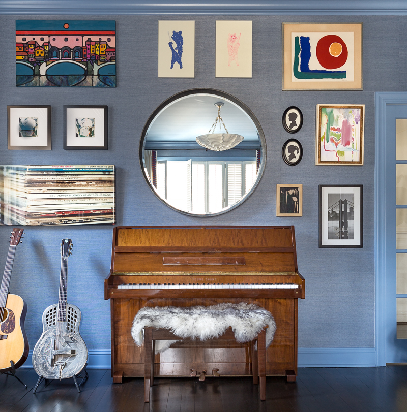 grasscloth living room, blue, gallery wall, guitar, sheepskin piano bench, plaster chandelier